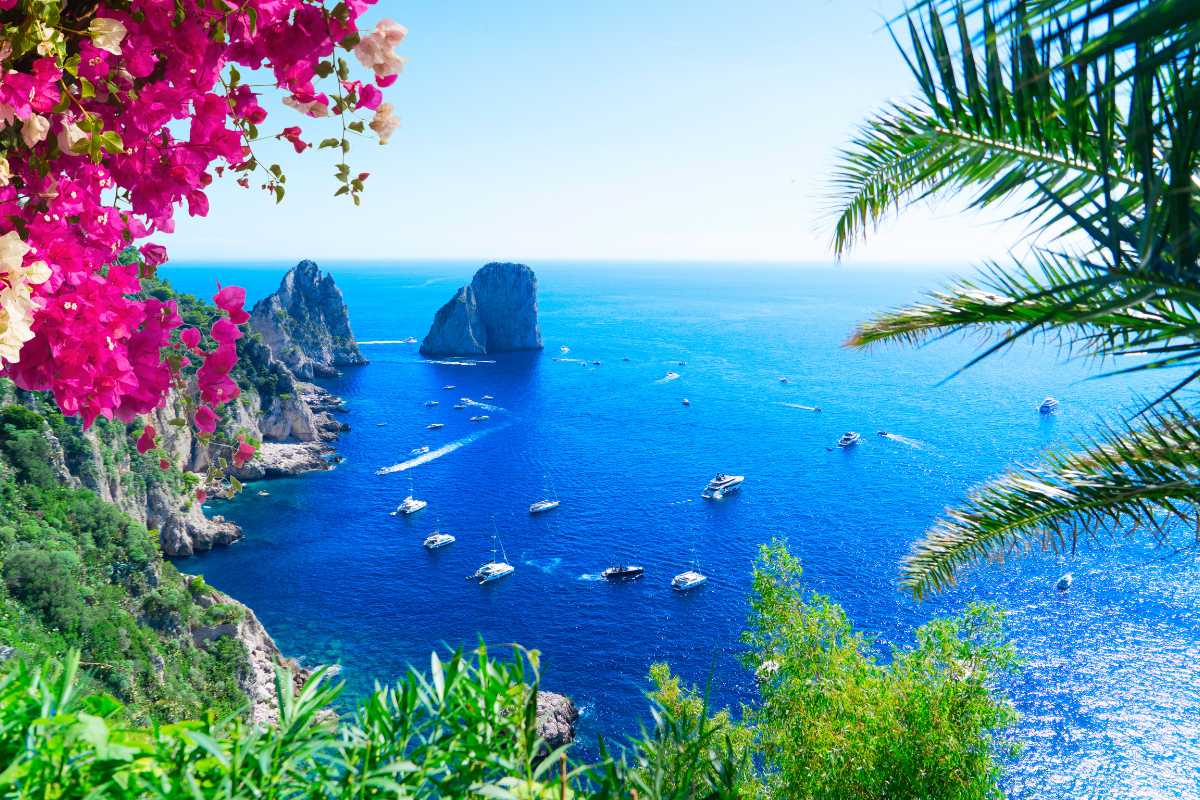 Dettaglio di una piattaforma in roccia sulla costa di Capri, bagnanti, ombrelloni colorati, Faraglioni in lontananza