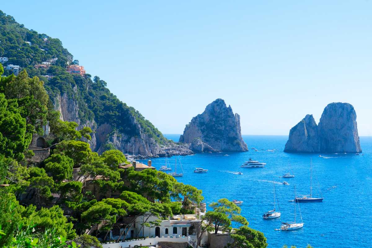 Vista panoramica delle spiagge di Capri al tramonto con i Faraglioni sullo sfondo, barche ormeggiate e bagnanti in relax